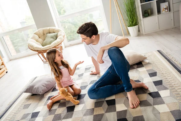 Full size photo of two cheerful peaceful people sit floor communicate say tell living room house indoors.