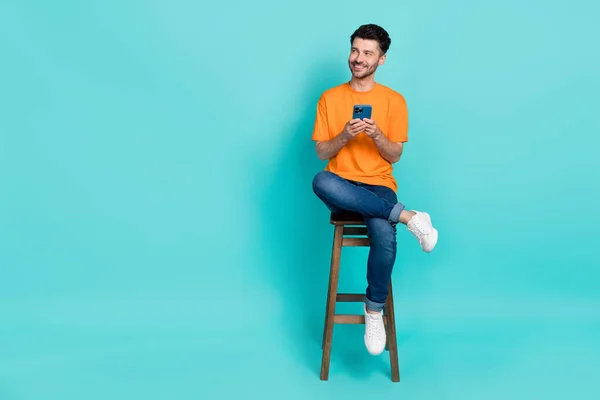 Full length photo of guy blogger sit chair using smart gadget look empty space isolated on aquamarine color background.