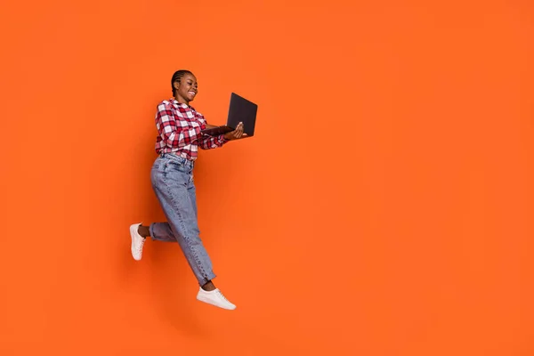 Full length photo of carefree excited person jump write email wireless netbook isolated on orange color background.