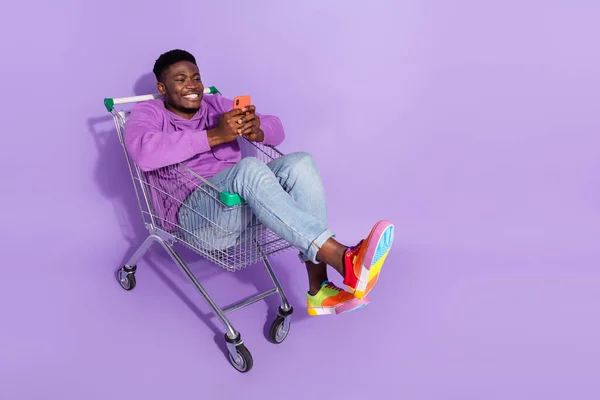 フルボディポートレートの面白い正男座ってトロリー使用電話ウェブサービス孤立した上に紫色の背景 — ストック写真