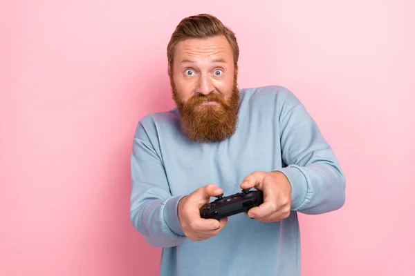 写真の正ハンサムな男とともに赤い髭を身に着けている青プルオーバー保持ジョイスティックトライ困難なレベルでピンク色の背景に隔離 — ストック写真