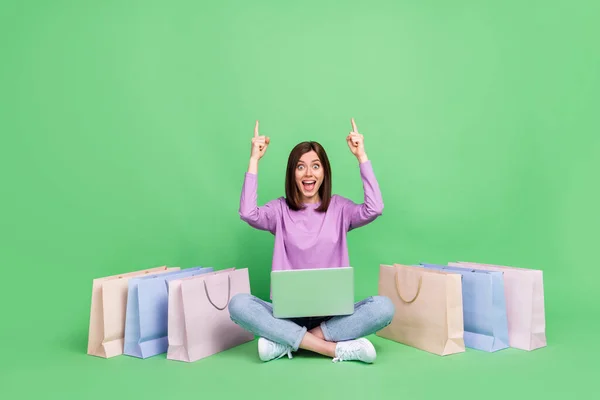全长照片 年轻迷人的女孩坐在疯狂包装的笔记本电脑上 网上购物手指指向空旷的空间广告 与绿色背景隔离 — 图库照片