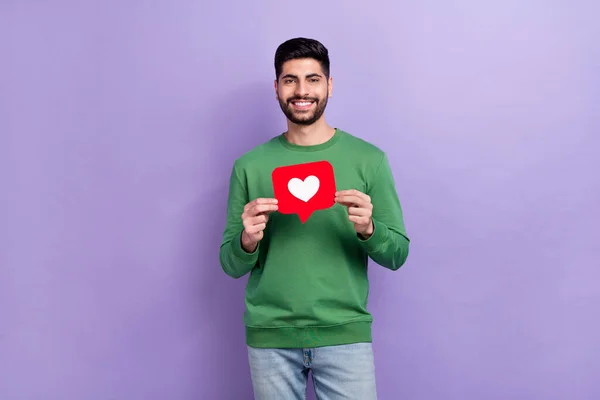 Photo of cheerful positive good mood man dressed green pullover hold heart in hands smiling got like isolated on violet color background.