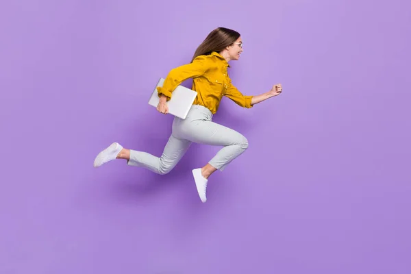 全长形象的疯狂精力充沛的女孩拿着上网本匆忙跳跃空旷的空间隔离在紫色的背景下 — 图库照片