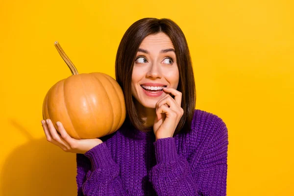 Photo of positive adorable minded lady hold pumpkin bite finger nail look empty space isolated on yellow color background.