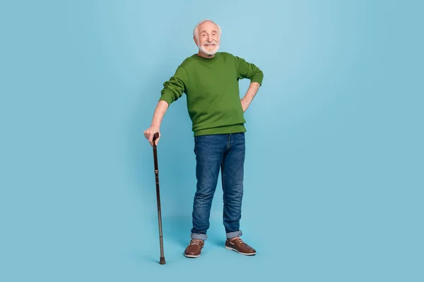 Full length portrait of satisfied friendly aged man hold stick put hand waist standing isolated on blue color background.