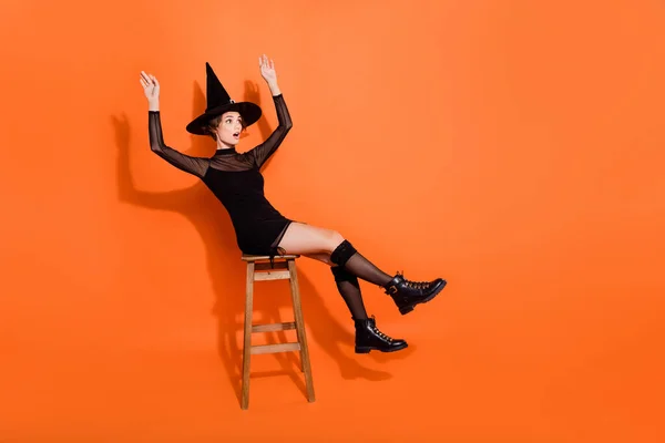 迷人的女士坐在椅子上失去平衡的全长照片 穿着时髦的黑色半身裙 衬托着橙色的背景 — 图库照片