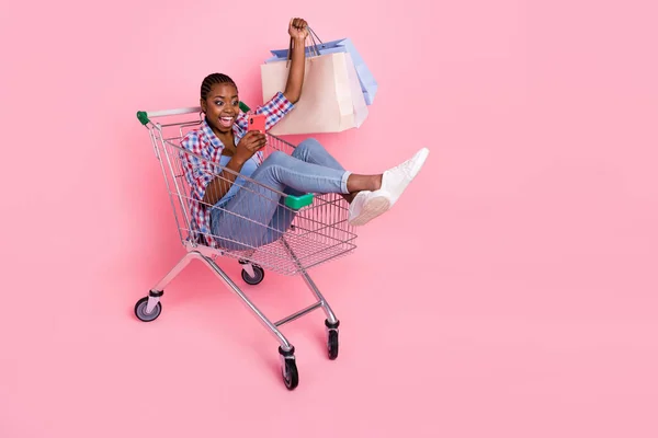 興奮魅力的な女の子のフルサイズの写真座ってスーパーマーケットトロリーホールドパッケージ使用電話でピンク色の背景 — ストック写真
