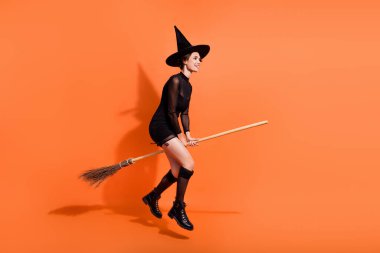 Full size photo of pretty woman flying broom sabbath shopping dressed trendy black halloween garment isolated on orange color background. clipart