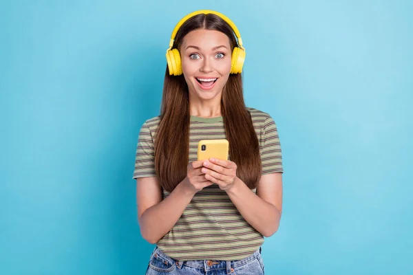 매력적 여성의 사진에는 헤드폰 노란색 스마트폰 충전기 기기가 파란색 배경에 — 스톡 사진