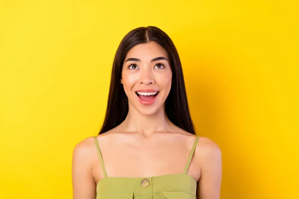 Portrait of astonished excited indonesian person look interested up empty space toothy smile isolated on yellow color background.