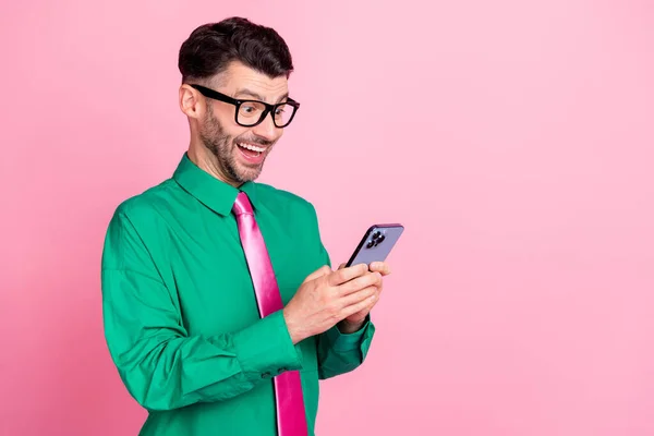 Photo of impressed funky guy wear green shirt spectacles typing modern device empty space isolated pink color background.