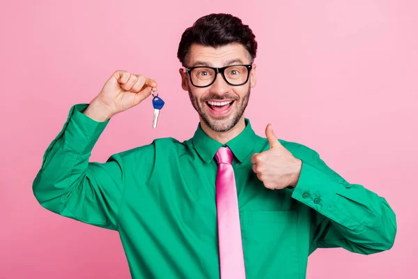 Photo of confident pretty guy wear green shirt spectacles rising keys showing thumb up isolated pink color background.