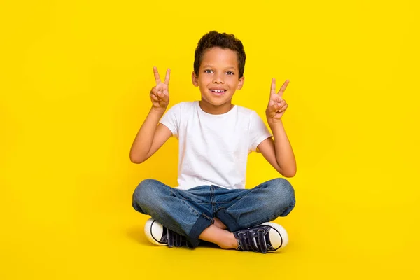 フルボディ写真の小さな男の子座ってショーV Sign摩耗Tシャツジーンズブーツ孤立した黄色の色の背景 — ストック写真