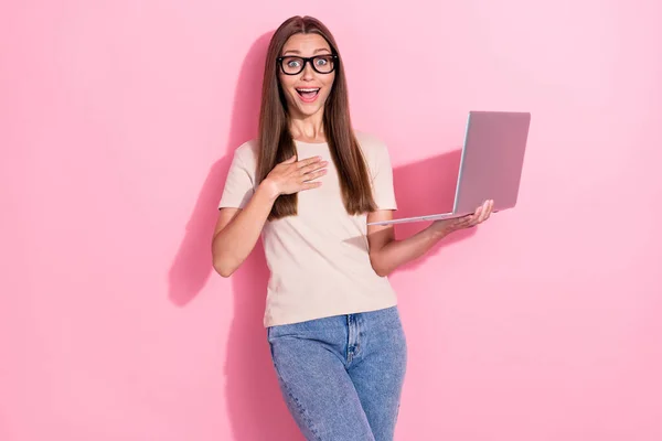 Photo of charming funny excited positive young girl wear glasses surprised winner lottery online bet hold computer isolated on pink color background.