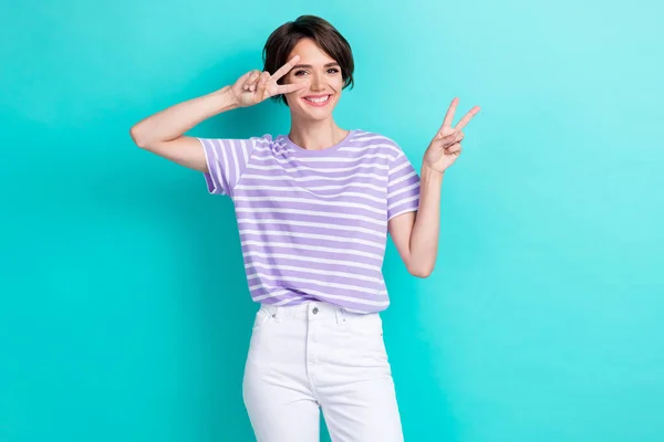 Photo of adorable sweet cherry lady arm demonstrate hi v symbol dressed striped clothes beaming grin isolated on cyan color background.