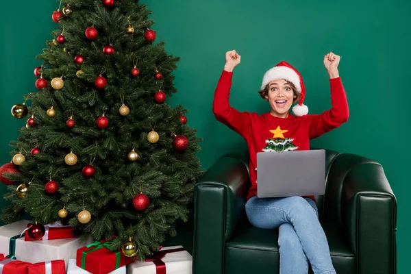 Portrait of cheerful satisfied person raise fists success achievement use netbook isolated on green color background.