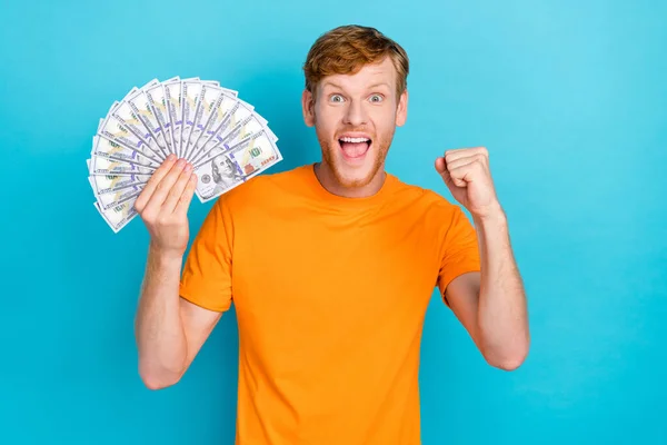 Photo of astonished ginger hair guy hold money yell wear orange t-shirt isolated on teal color background.