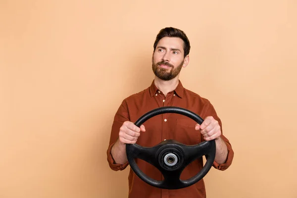 Portrait of minded positive man arms hold wheel look interested empty space isolated on beige color background.