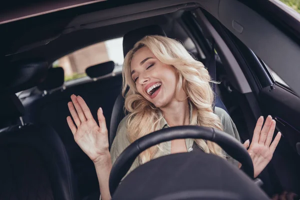 Portrait of attractive cheerful dreamy wavy haired girl sitting in car riding singing enjoying comfortable trip new modern vehicle outdoors.