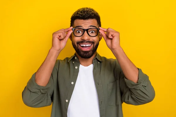 Photo of attractive excited man wear khaki shirt arms spectacles smiling isolated yellow color background.