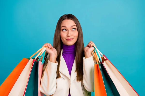 Photo of charming suspicious mischief girl arm hold stylish purchase consider plan eyes up empty space isolated on blue color background.