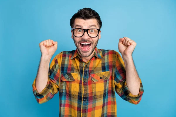 Photo of impressed astonished ecstatic man wear glasses plaid shirt hold hands up screaming yes isolated on blue color background.