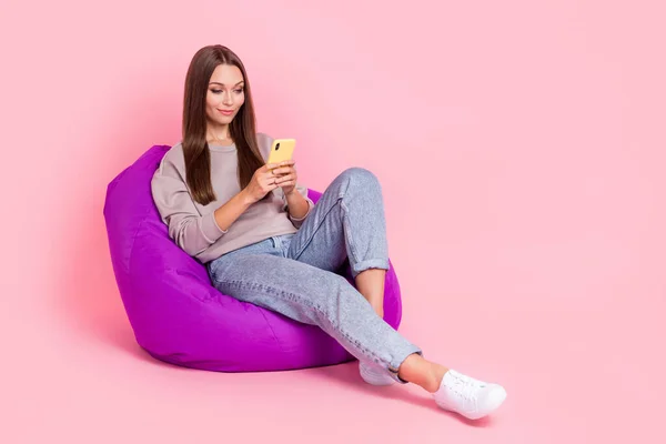 美しい平和的な人の完全な長さの肖像画座って快適バッグホールド使用電話でピンク色の背景 — ストック写真