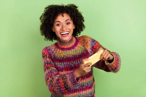 写真のファンキーな若い巻き毛の女性のプレイ電話は緑の色の背景に隔離された赤いセーターを着用 — ストック写真
