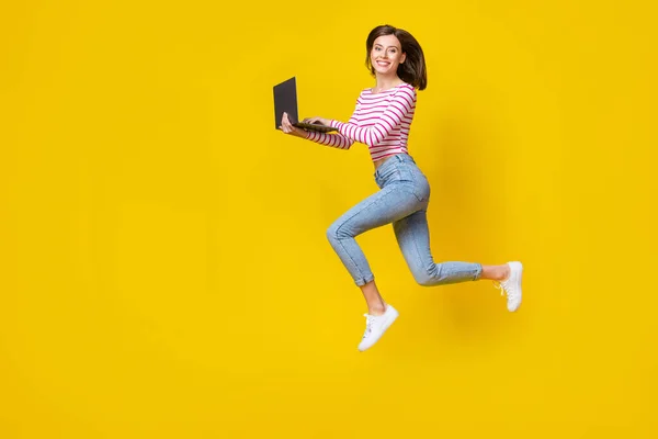 年轻美女跑步的全长照片 手持笔记本电脑 穿着时髦的条纹衣服 背景是黄色的 — 图库照片
