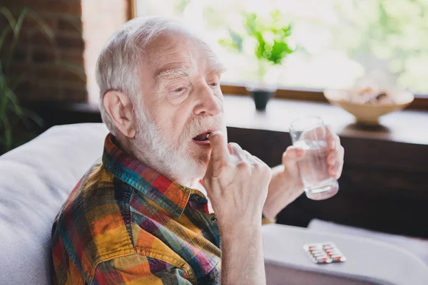 身穿格子花衬衫的心烦意乱的退休男子坐在沙发上 在室内喝水的照片 — 图库照片