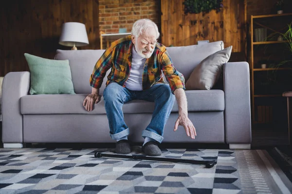 Photo of tired lonely man pensioner wear checkered shirt trying standing up sofa falling walking cane indoors house room.