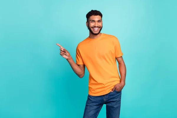 照片上的心情很好 可爱的男人穿着橙色的T恤 微笑着指指点点空旷的空间孤立的绿松石色背景 — 图库照片