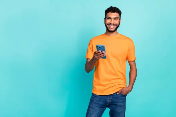 照片上 有自信迷人的男人穿着橙色T恤 Sms现代设备 空旷的空间 孤立的蓝绿色背景 — 图库照片