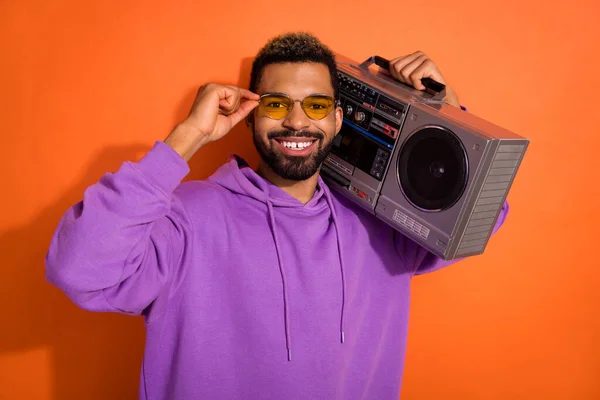 Portrait of cheerful excited person hand touch sunglass carry boombox isolated on orange color background.