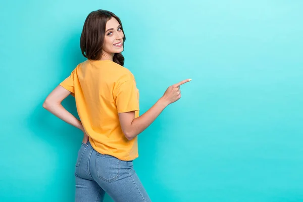若い愛らしいかわいい素敵な女の子の写真は スタイリッシュなジーンズTシャツの指ポイント空のスペース広告を身に着けていますキャドルの後ろに隔離されたアクアマリン色の背景 — ストック写真