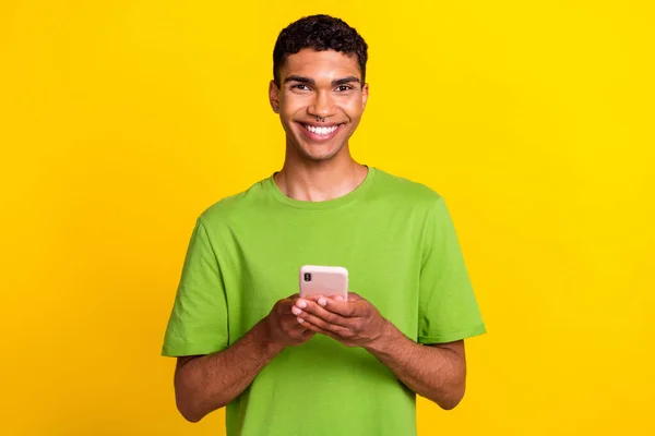 年轻英俊的学生穿着绿色T恤衫的照片拿着新的智能手机流行博主的影响者被黄色背景隔离 — 图库照片