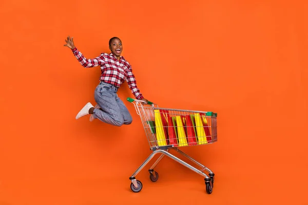 クレイジーエネルギッシュな女の子ジャンプの完全な長さは楽しい時間ショッピングを楽しんでいますオレンジ色の背景に隔離 — ストック写真