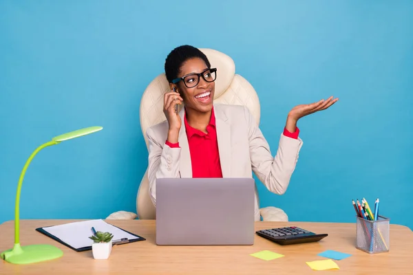 Portrait of busy boss person sit workplace speak communicate cellphone isolated on blue color background.