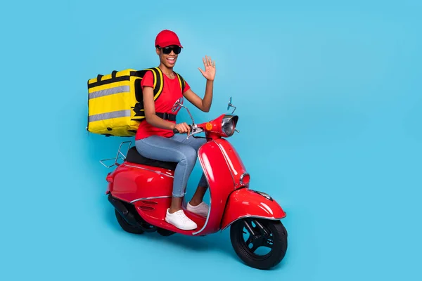 Photo of friendly funky short hair human wear red uniform moped rider fast food delivery waving arm isolated blue color background.