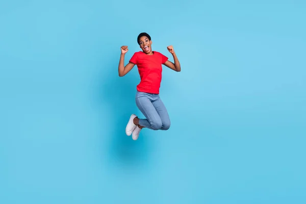 Photo of lucky excited short hair human wear red t-shirt jumping high rising fists isolated blue color background.