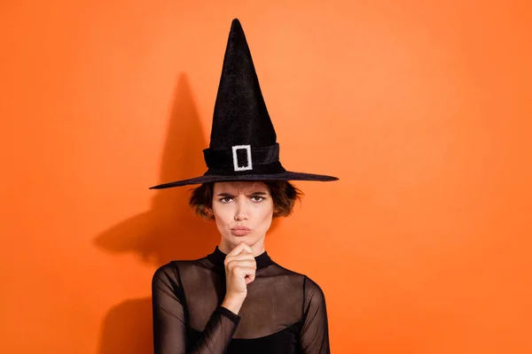 Photo portrait of stunning young woman frowning pensive argument dressed trendy black halloween witch look isolated on orange background.