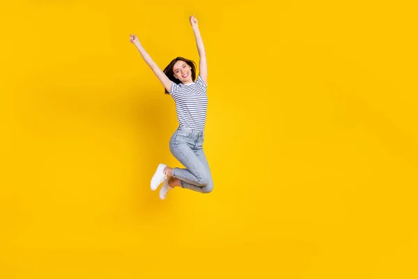 フルサイズ写真の活動的な若い女性の上昇拳お祝いウィン宝くじジャンプは黄色の色の背景に隔離されたスタイリッシュなストライプの外観を着用 — ストック写真