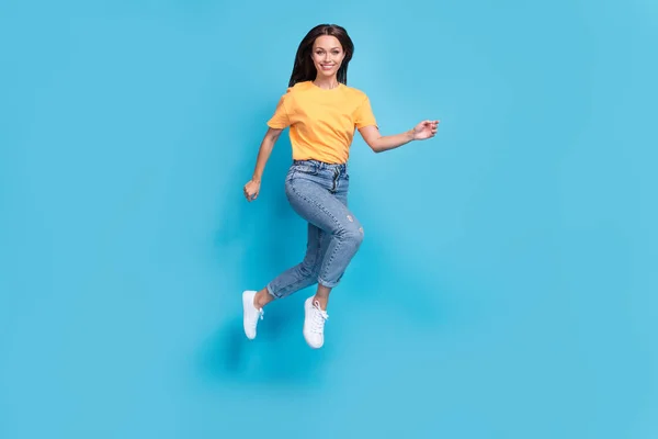 フル長さ写真のかなり興奮した女性着用黄色Tシャツジャンプ高い実行中の高速隔離された青の色の背景 — ストック写真