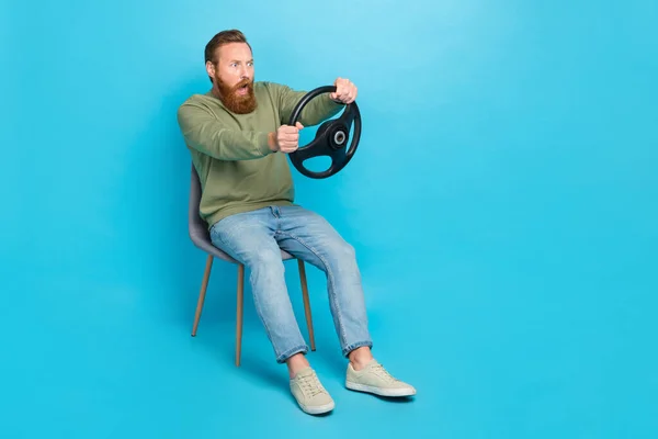 Full size photo of frightened man red hairstyle wear khaki pullover hold steering wheel look empty space isolated on blue color background.