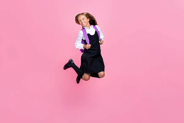 フルサイズ写真の面白いです遊び心のある正の女の子とともにブロンド髪ドレス学校制服ジャンプ楽しいですピンク色の背景に孤立 — ストック写真