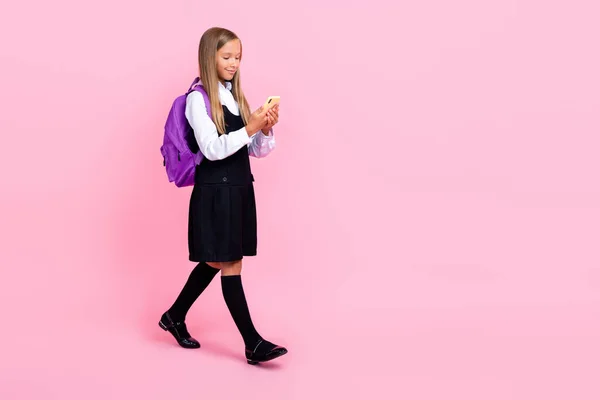 全长照片 年轻可爱的小女生穿着校服 用智能手机沉迷背包回到学校空旷的空间 用粉色背景隔开 — 图库照片