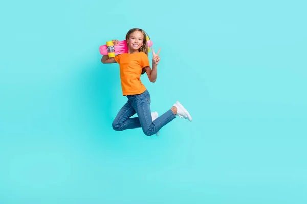 かわいい小さな子供の完全な長さの写真は オレンジ色のTシャツを着てロングボードジャンプを保持するVサイン隔離されたターコイズ色の背景を示す — ストック写真