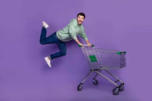 クレイジー屈託のない人の完全な体の肖像ジャンプフライプッシュショッピングトロリーは紫の色の背景に隔離 — ストック写真