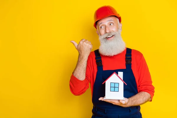 Photo of excited dreamy old guy dressed uniform overall red hardhat thumb empty space home developing isolated yellow color background.